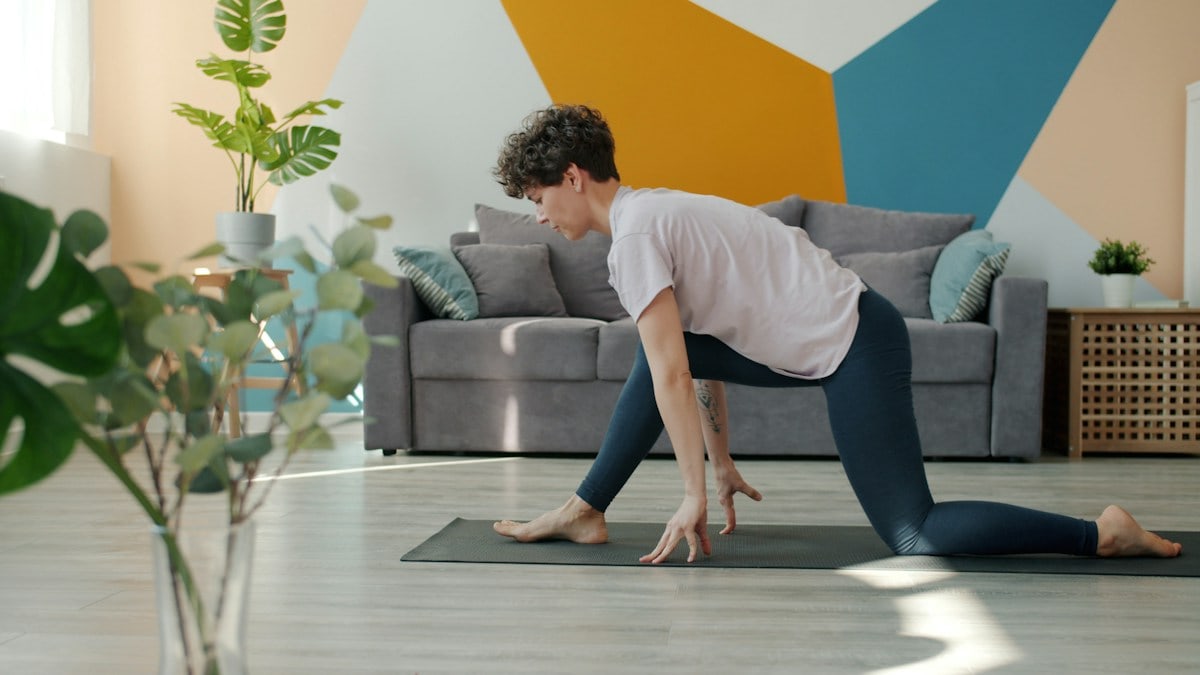 Flexible young woman is doing yoga in house practising asanas alone on comfy mat enjoying useful activity. Indoor sports, active lifestyle and modern youth concept.